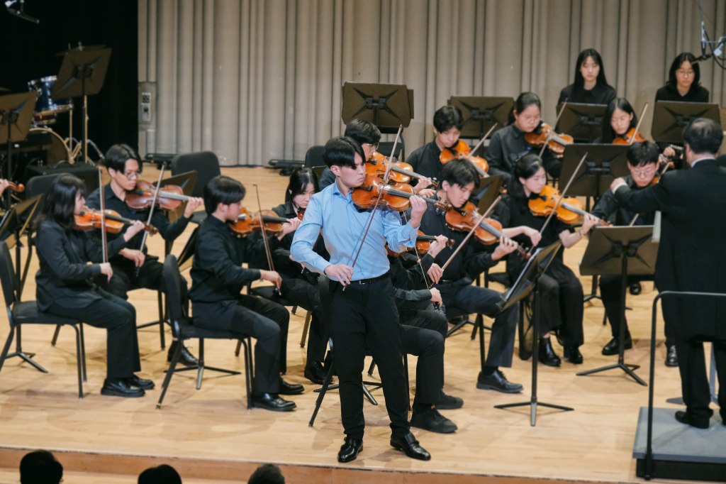 Violin soloist performing on stage with youth orchestra. 